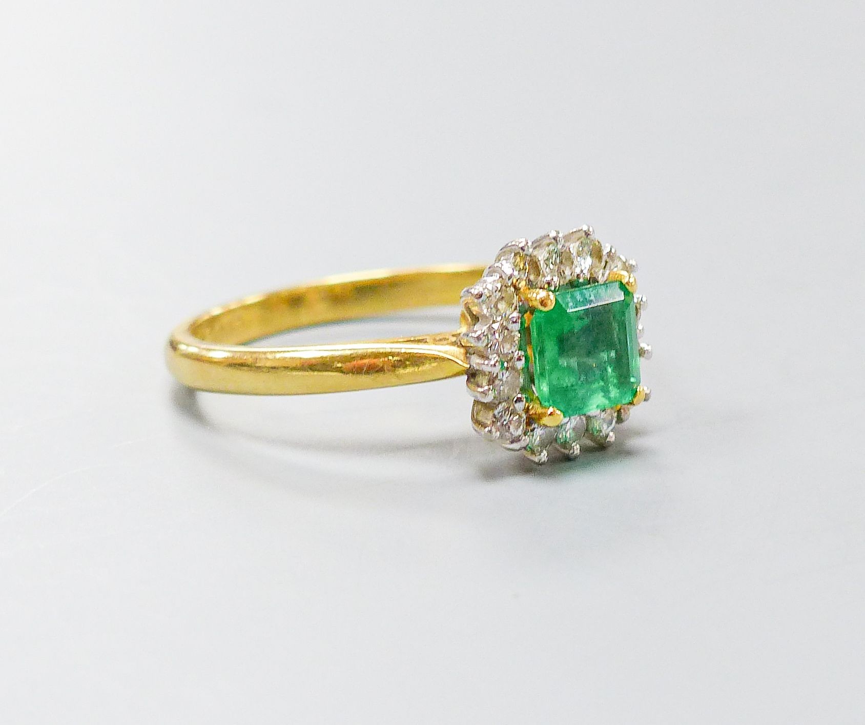 A modern 18ct gold, emerald and diamond set square cluster ring, size O, gross weight 4.3 grams.